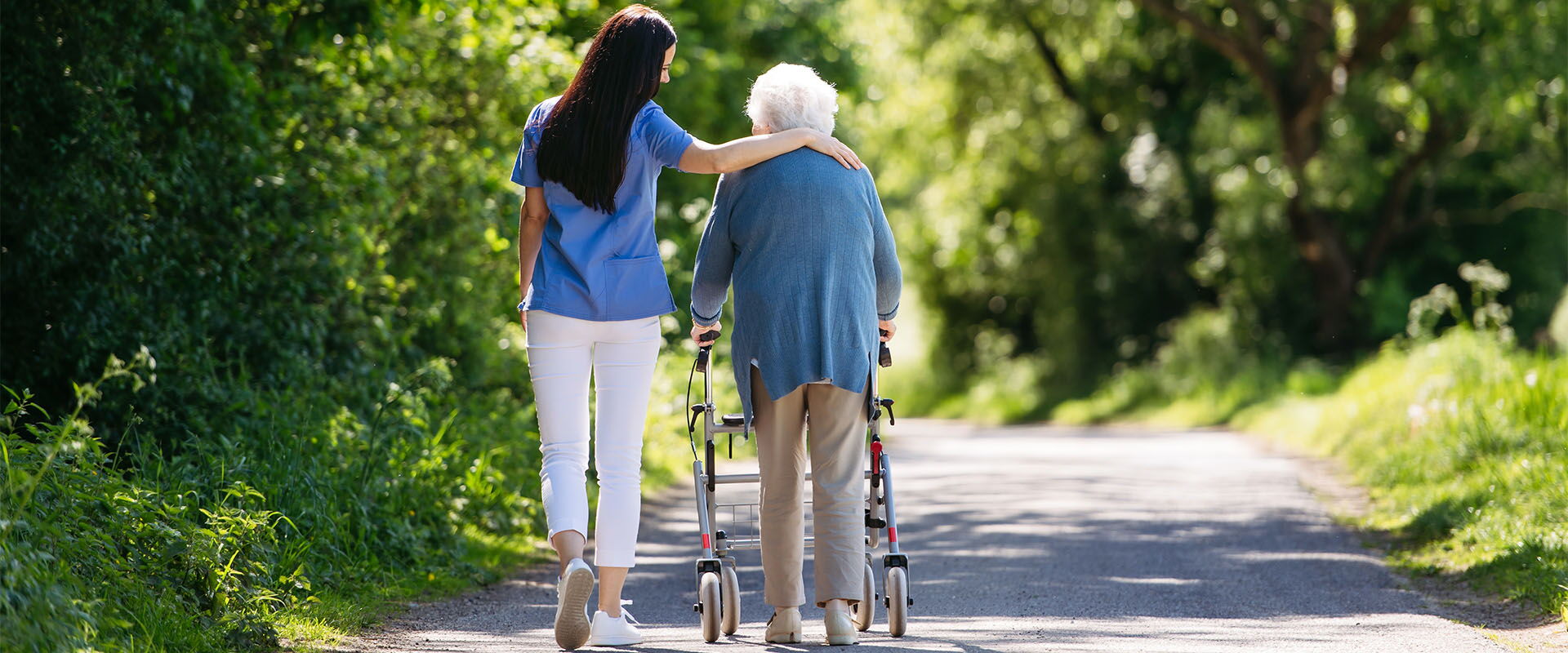 Pflegerin geht mit einer Seniorin im Wald Spazieren